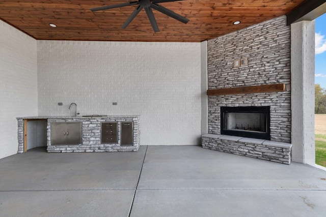 view of patio with a fireplace, ceiling fan, and exterior kitchen