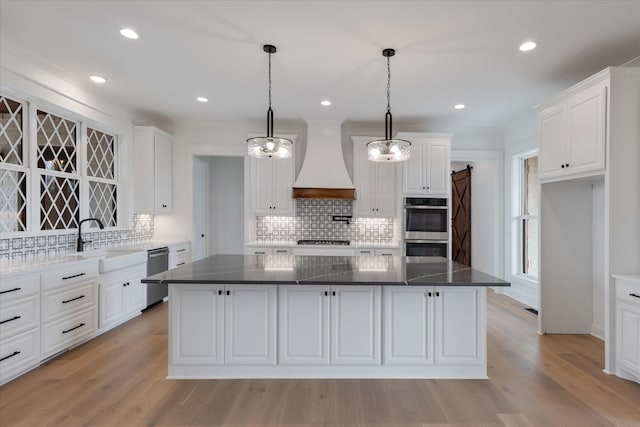 kitchen featuring a center island, a barn door, white cabinetry, custom range hood, and stainless steel appliances