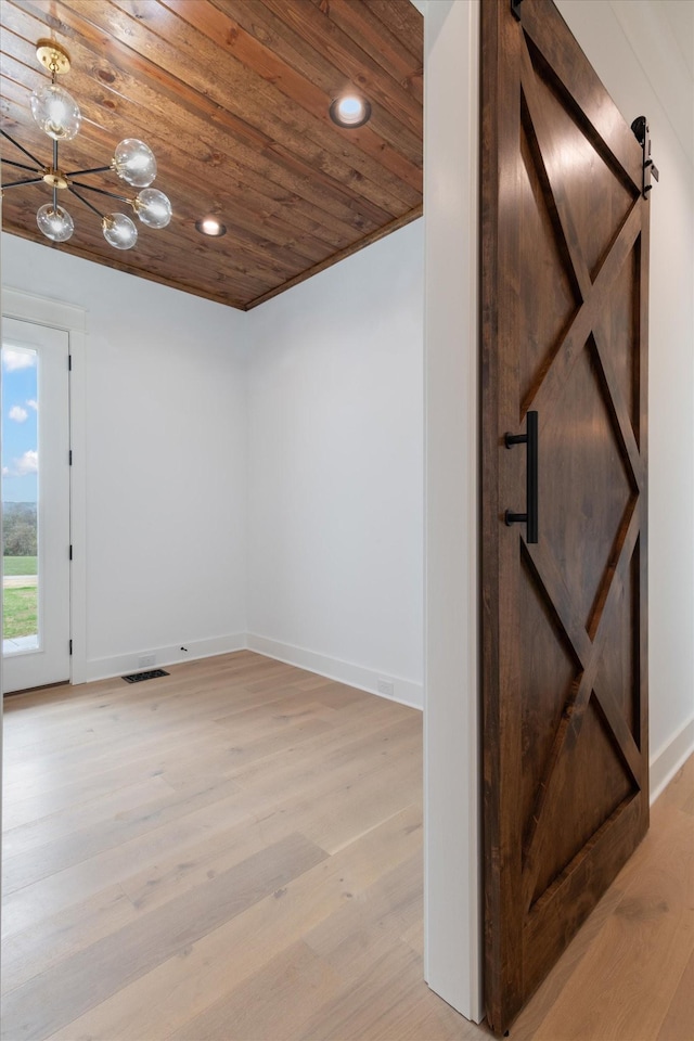 empty room featuring a barn door, wood ceiling, and light hardwood / wood-style flooring