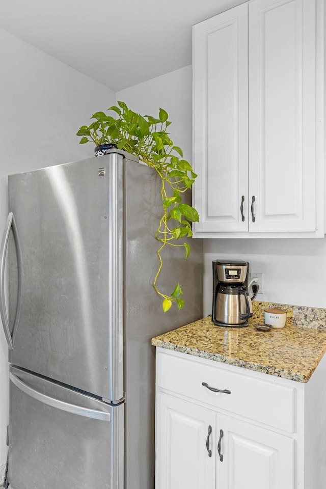 kitchen featuring white cabinets, stainless steel refrigerator, and light stone countertops