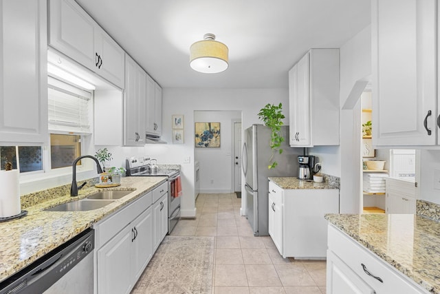 kitchen with appliances with stainless steel finishes, light stone counters, sink, light tile patterned floors, and white cabinetry