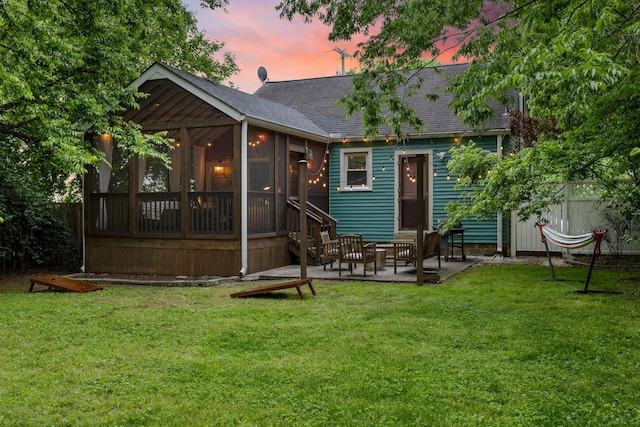 back house at dusk with a sunroom, a patio area, and a yard