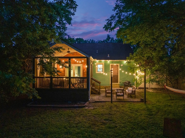 back house at dusk with a lawn and a patio