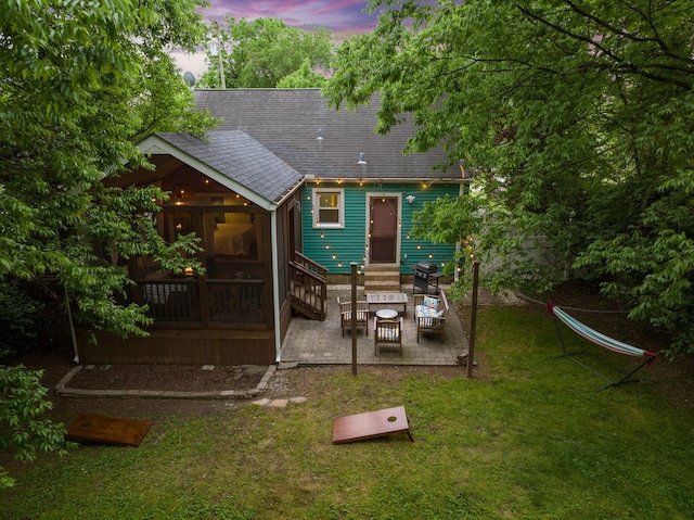 back house at dusk with a yard, a patio area, and a sunroom