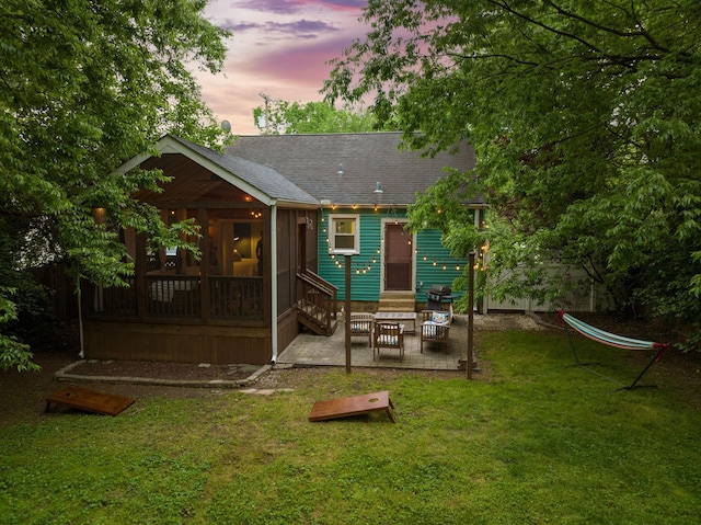 back house at dusk featuring a lawn, a sunroom, and a patio