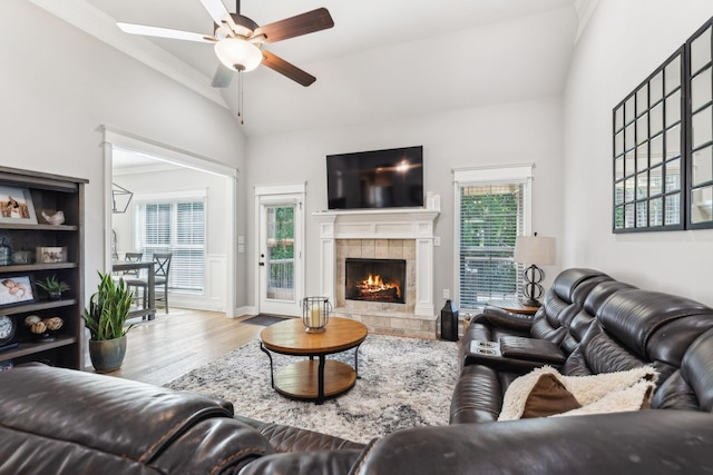 living room featuring vaulted ceiling, ceiling fan, ornamental molding, a fireplace, and light hardwood / wood-style floors