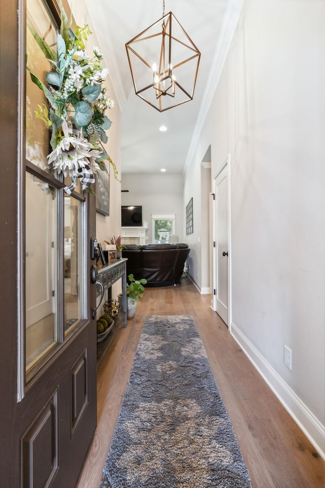 entryway featuring a tile fireplace, hardwood / wood-style flooring, an inviting chandelier, and crown molding