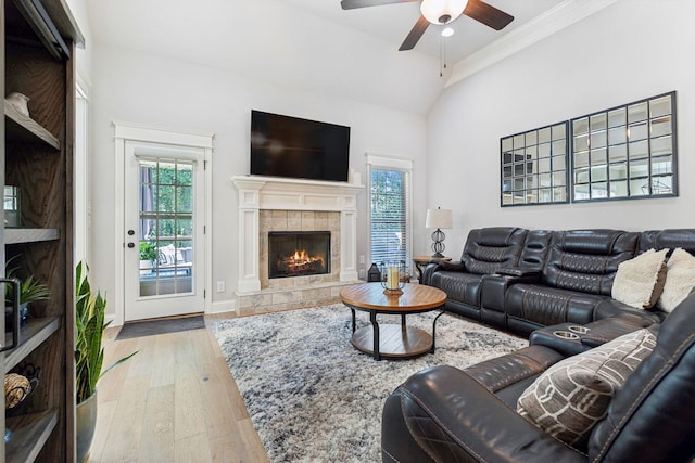 living room with crown molding, vaulted ceiling, ceiling fan, wood-type flooring, and a tiled fireplace