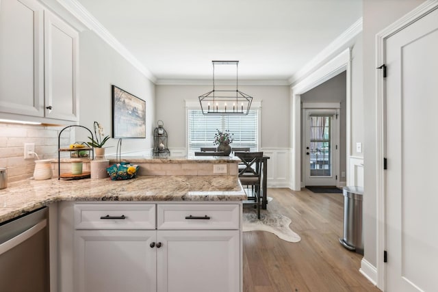 kitchen featuring light stone countertops, white cabinetry, hanging light fixtures, stainless steel dishwasher, and light hardwood / wood-style floors