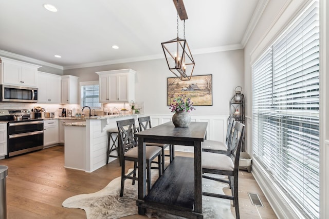 dining space with light wood-type flooring, an inviting chandelier, ornamental molding, and sink