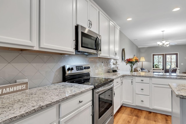 kitchen with white cabinetry, sink, stainless steel appliances, light stone counters, and a chandelier