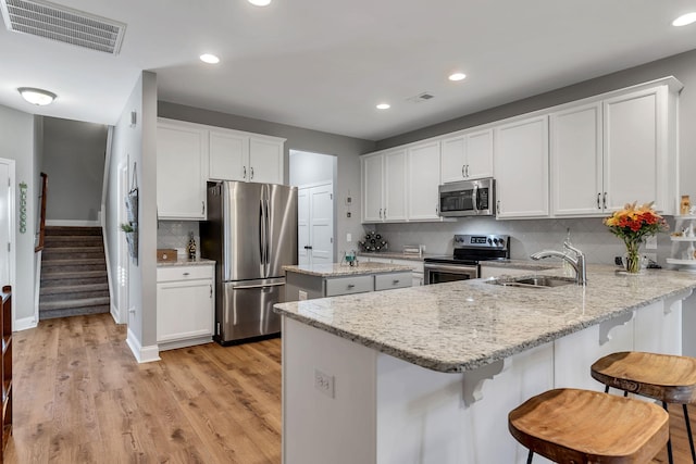 kitchen with sink, decorative backsplash, light stone countertops, appliances with stainless steel finishes, and kitchen peninsula