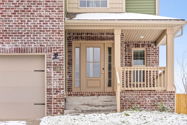 snow covered property entrance with covered porch and a garage