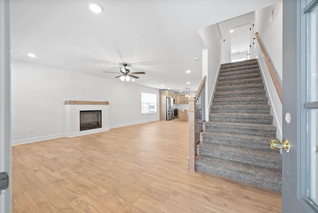 stairway featuring hardwood / wood-style flooring, a brick fireplace, and ceiling fan