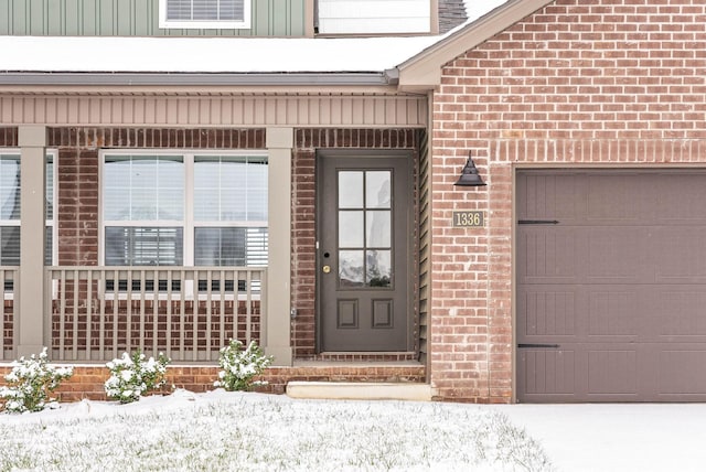 snow covered property entrance with a porch and a garage