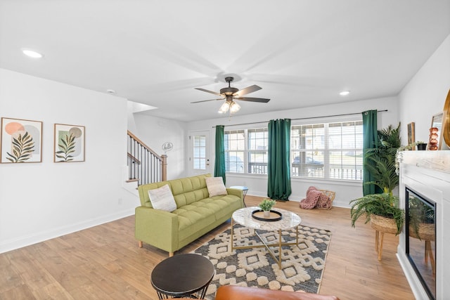 living area with a wealth of natural light, light wood-type flooring, a glass covered fireplace, and stairs