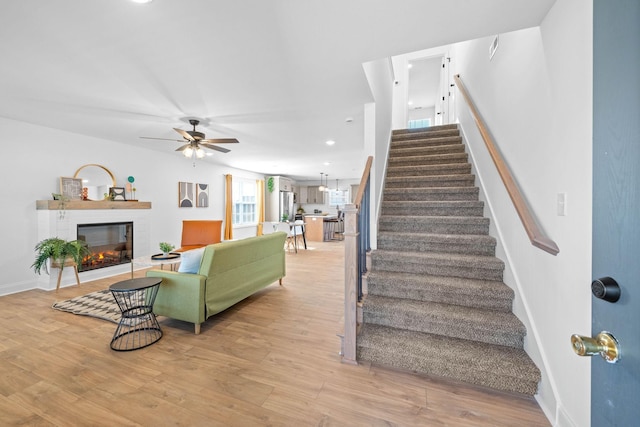 interior space with a ceiling fan, a glass covered fireplace, baseboards, and wood finished floors