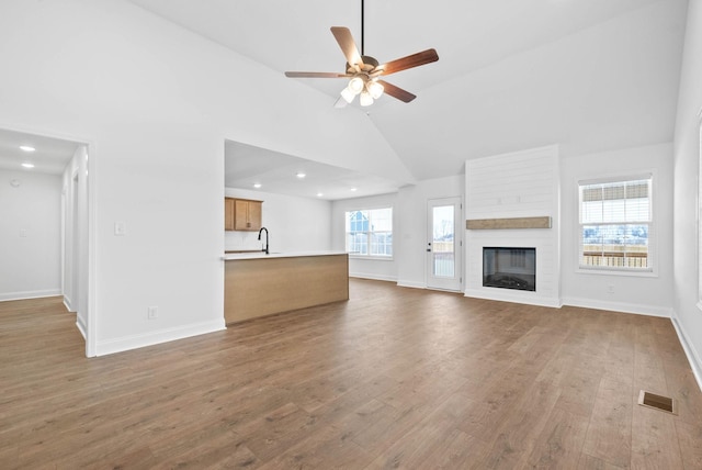 unfurnished living room featuring ceiling fan, sink, high vaulted ceiling, wood-type flooring, and a fireplace