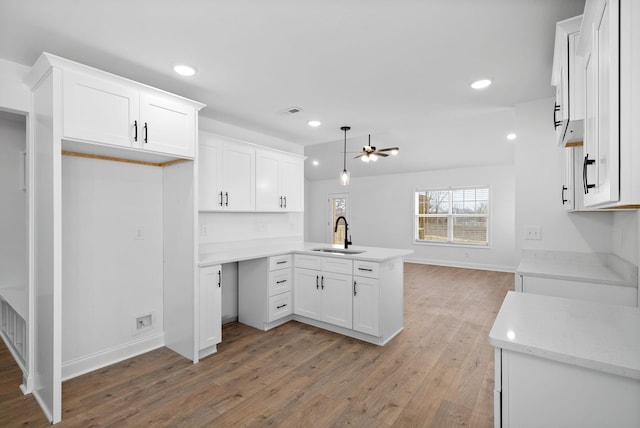 kitchen featuring light wood-style flooring, open floor plan, a peninsula, white cabinetry, and a sink