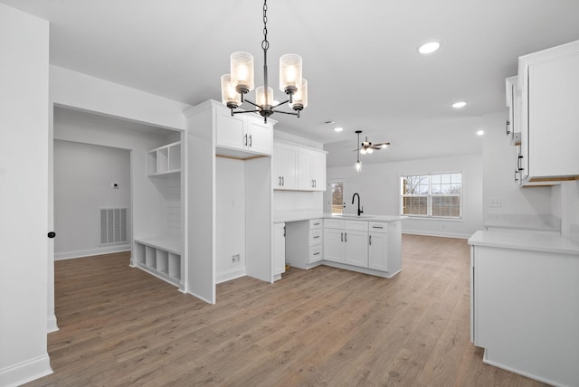 kitchen featuring light countertops, visible vents, light wood-style flooring, a sink, and a peninsula