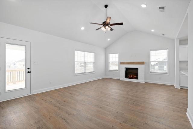 unfurnished living room featuring lofted ceiling, ceiling fan, a warm lit fireplace, hardwood / wood-style flooring, and visible vents