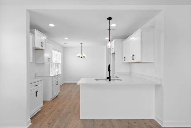 kitchen with a peninsula, a sink, light wood-style flooring, and white cabinets