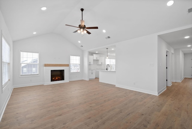 unfurnished living room with light wood finished floors, vaulted ceiling, and a sink