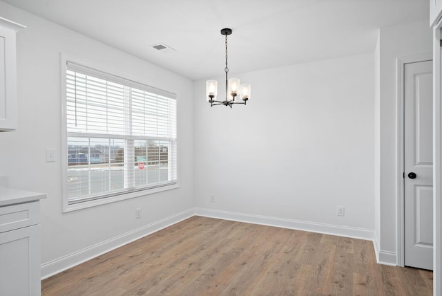 unfurnished dining area with baseboards, light wood-style floors, visible vents, and a notable chandelier