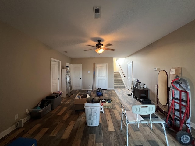 living room with a textured ceiling, ceiling fan, and dark wood-type flooring