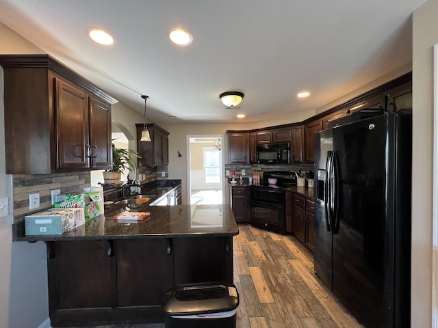 kitchen with hanging light fixtures, kitchen peninsula, a breakfast bar area, dark brown cabinets, and black appliances