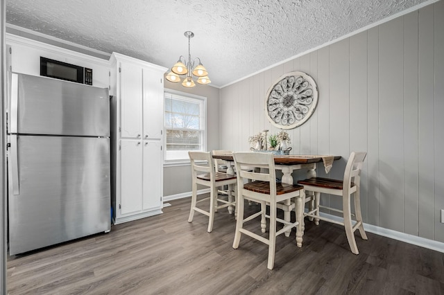 dining room with a textured ceiling, wooden walls, crown molding, light hardwood / wood-style flooring, and a chandelier