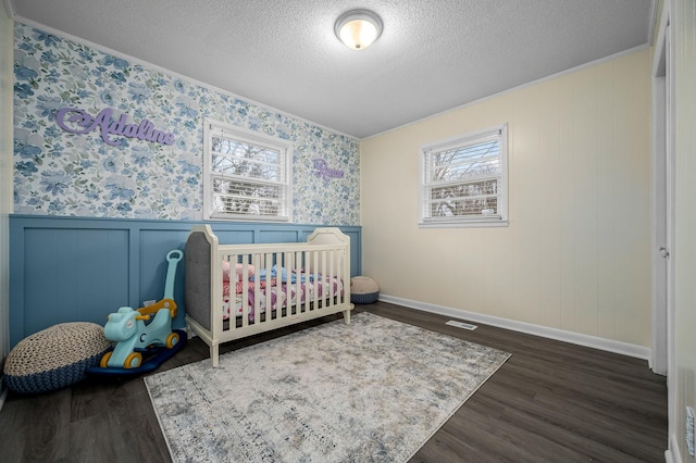 bedroom featuring a textured ceiling, crown molding, dark wood-type flooring, and a nursery area