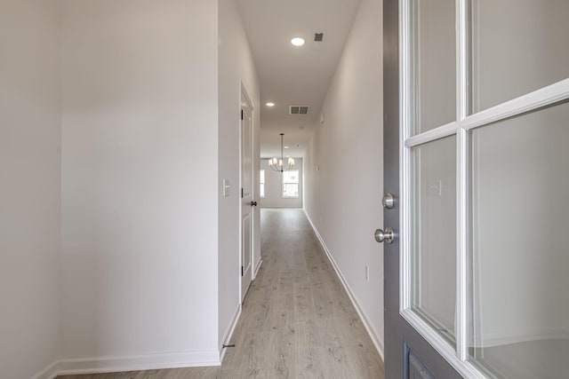 corridor featuring an inviting chandelier and light hardwood / wood-style flooring