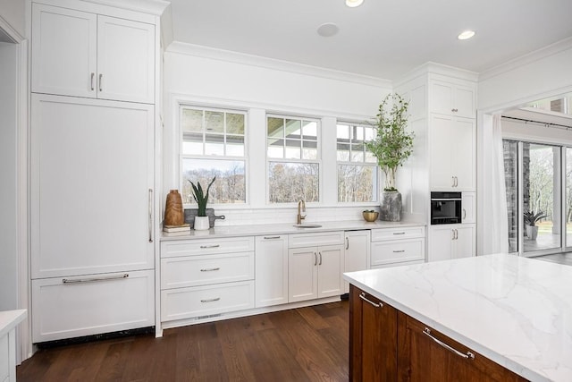 kitchen with light stone countertops, ornamental molding, sink, white cabinets, and dark hardwood / wood-style floors