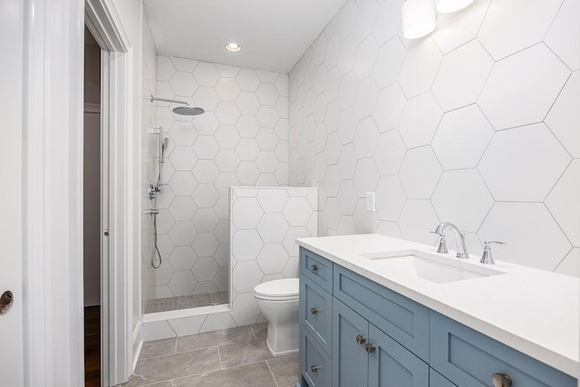 bathroom featuring a tile shower, vanity, toilet, and tile walls