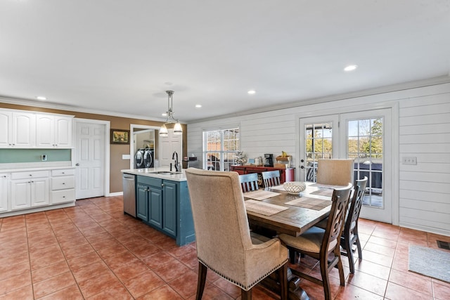 dining room with sink, wooden walls, ornamental molding, and light tile patterned floors