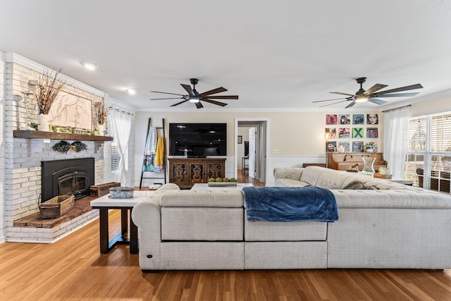 living room featuring wood-type flooring, a brick fireplace, ceiling fan, and crown molding