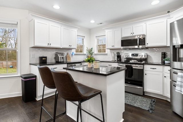 kitchen featuring a healthy amount of sunlight, white cabinets, appliances with stainless steel finishes, a kitchen island, and dark hardwood / wood-style flooring