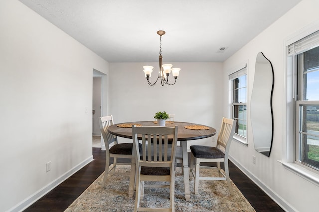 dining space with dark wood-type flooring and an inviting chandelier