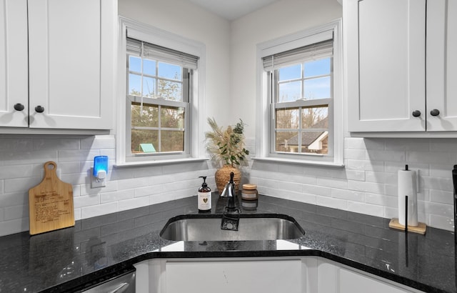 kitchen featuring backsplash, white cabinets, sink, stainless steel dishwasher, and dark stone countertops