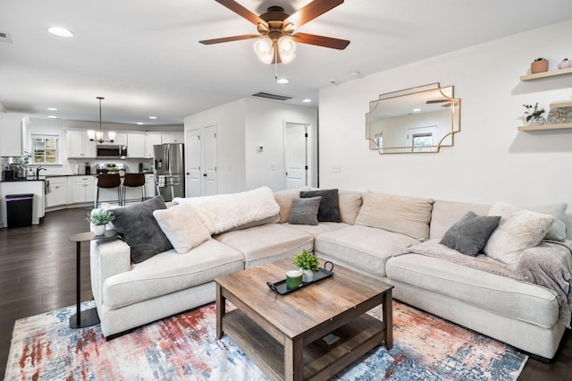 living room with dark wood-type flooring and ceiling fan with notable chandelier