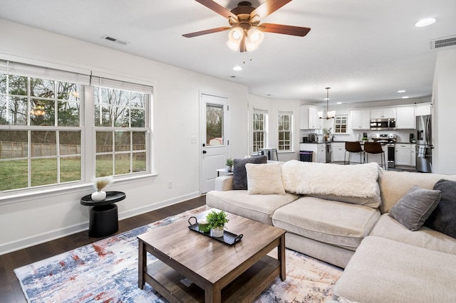 living room featuring ceiling fan with notable chandelier and dark wood-type flooring