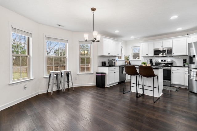 kitchen featuring a kitchen bar, appliances with stainless steel finishes, pendant lighting, a notable chandelier, and white cabinets