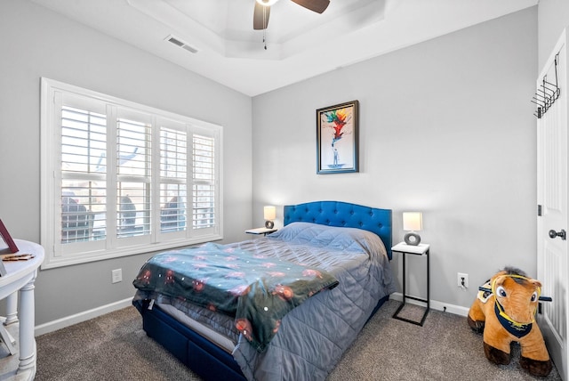 bedroom featuring dark colored carpet, ceiling fan, a tray ceiling, and multiple windows