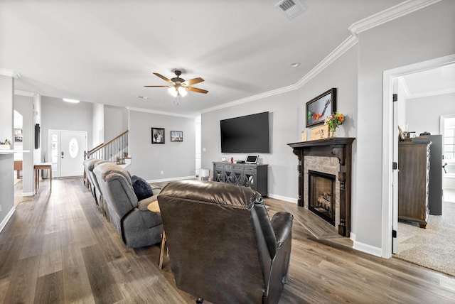 living room featuring ceiling fan, hardwood / wood-style flooring, crown molding, and a stone fireplace