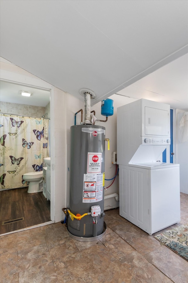 utility room with water heater and stacked washer and clothes dryer