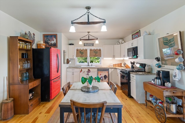 kitchen with pendant lighting, white cabinets, black appliances, and light hardwood / wood-style flooring