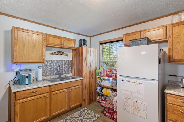 kitchen with a textured ceiling, white fridge, crown molding, and sink