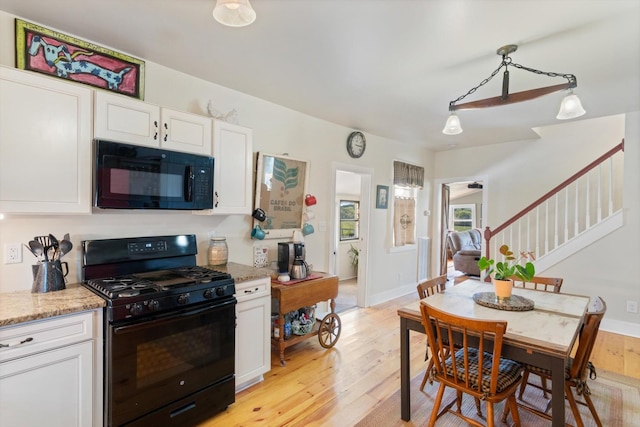 kitchen with light stone counters, pendant lighting, light hardwood / wood-style floors, white cabinets, and black appliances