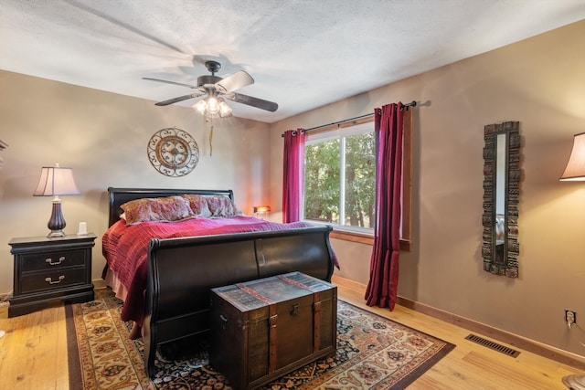 bedroom with ceiling fan, light hardwood / wood-style floors, and a textured ceiling